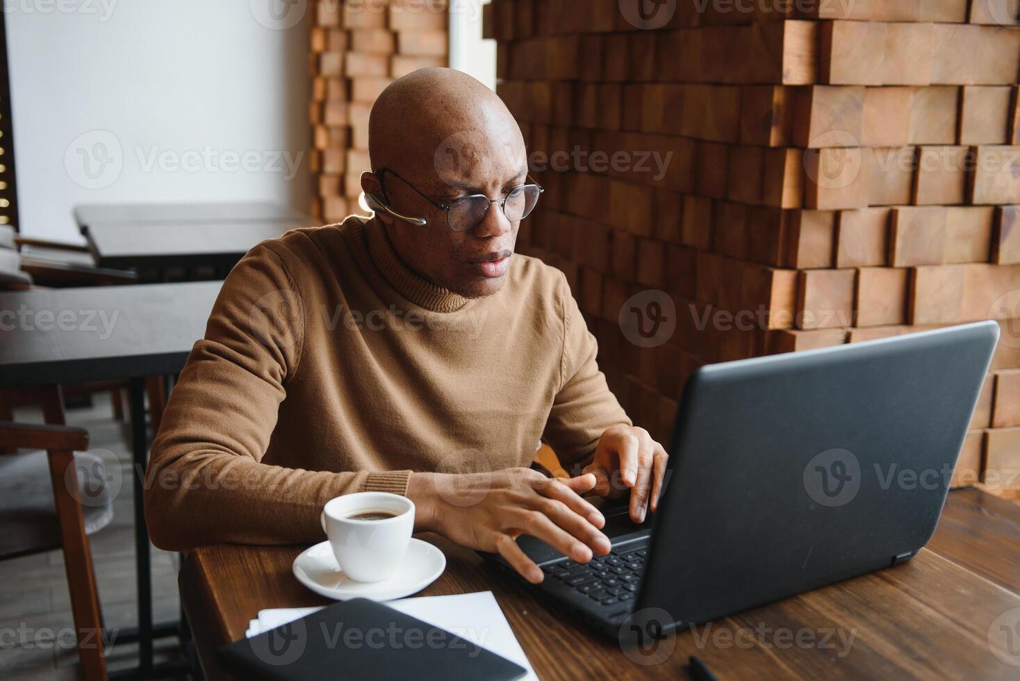 Focused african man wearing headphones watching webinar training making notes study online learning language on computer, black male student looking at laptop elearning in internet write information. photo