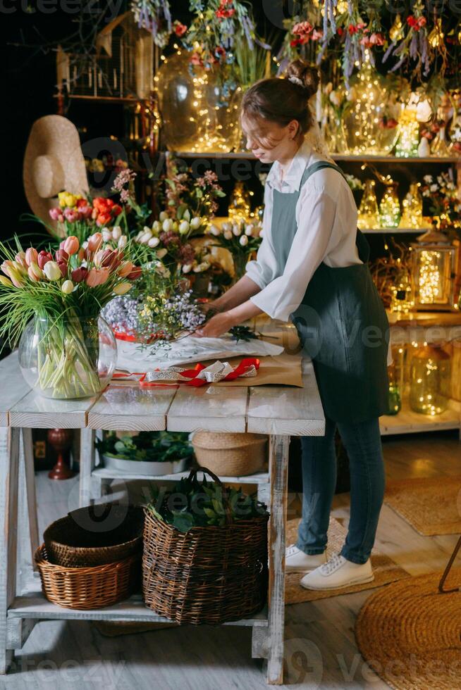 un mujer en su florista tienda recoge ramos de flores de flores el concepto de un pequeño negocio. ramos de flores de tulipanes para el fiesta en marzo 8. foto