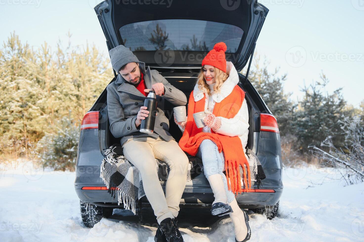 Pareja en amor sentado en coche maletero Bebiendo caliente té en Nevado invierno bosque y charlando personas relajante al aire libre durante la carretera viaje. san valentin día foto