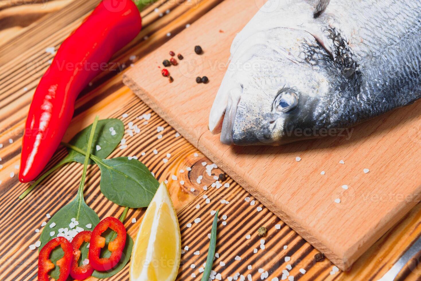 Fresh raw dorado fish. Sea bream, lying on a wooden board on a table with herbs and salt and spices. Dorado and ingredients for cooking on the table. Close-up photo