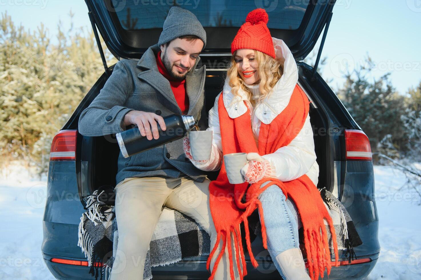 Pareja en amor sentado en coche maletero Bebiendo caliente té en Nevado invierno bosque y charlando personas relajante al aire libre durante la carretera viaje. san valentin día foto