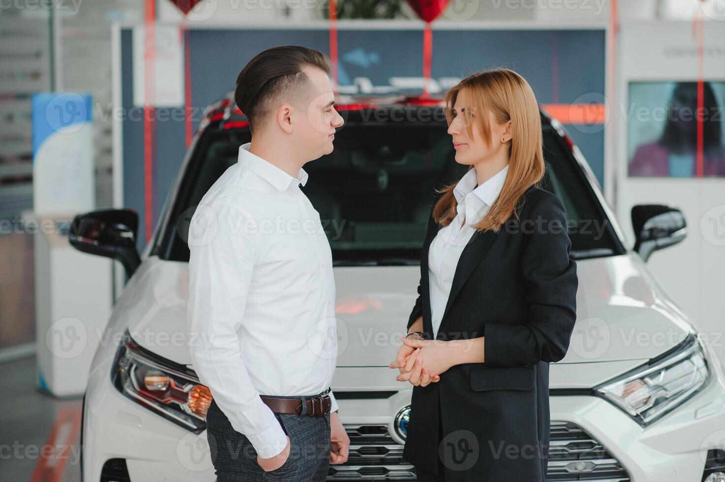 Happy young couple chooses and buying a new car for the family in the dealership photo