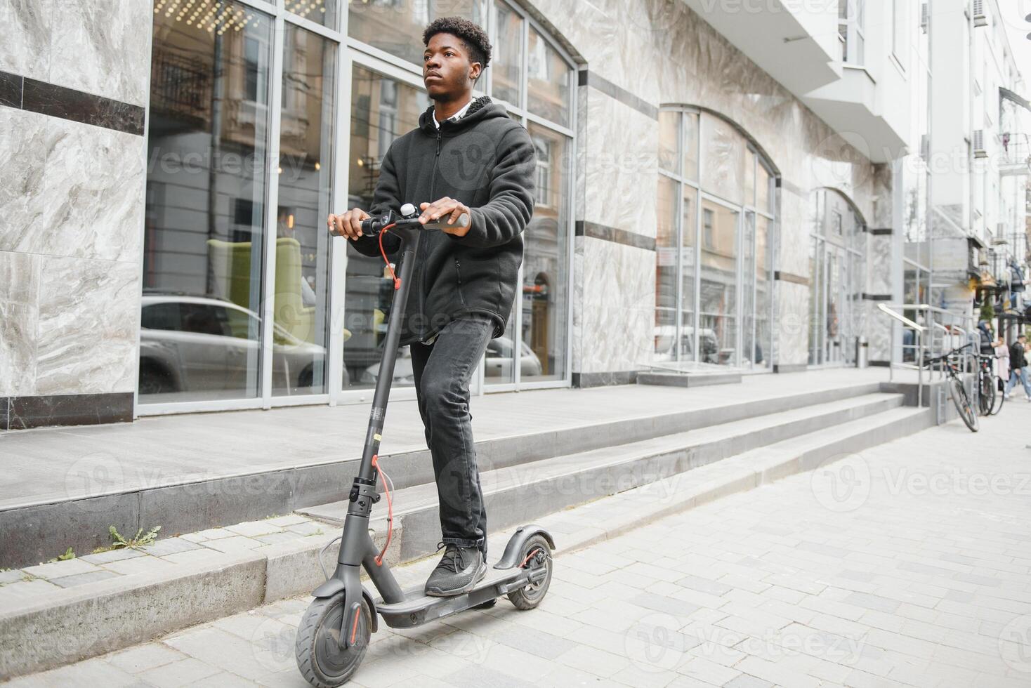 lleno cuerpo lado retrato contento africano americano hombre en móvil scooter en calle foto