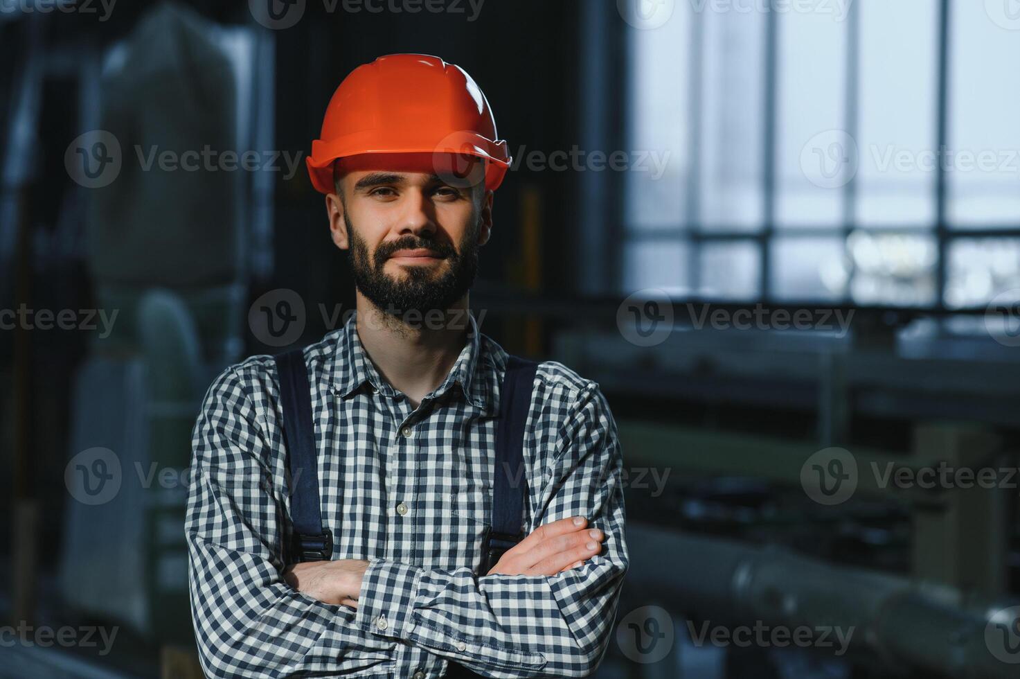 Portrait of Professional Heavy Industry Engineer Worker Wearing Safety Uniform, Hard Hat Smiling. In the Background Unfocused Large Industrial Factory. photo