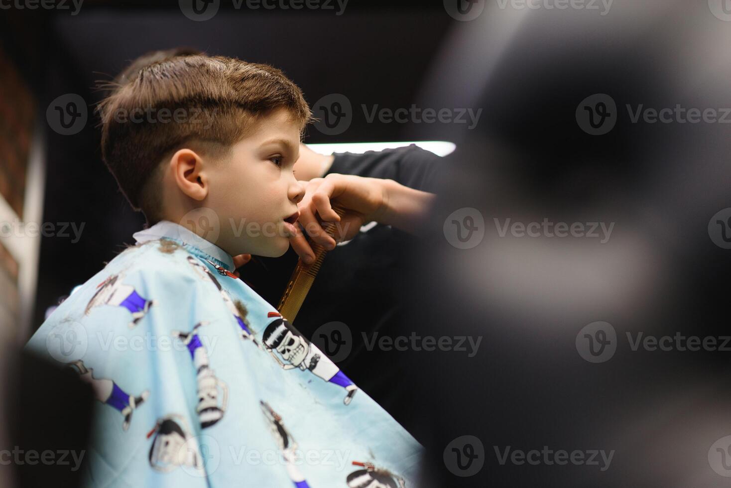 un pequeño linda chico se sienta en un peluquería a el estilista, un alumno es consiguiendo pelo cortar en un belleza salón, un niño a un barberías, un corto de los hombres Corte de pelo foto