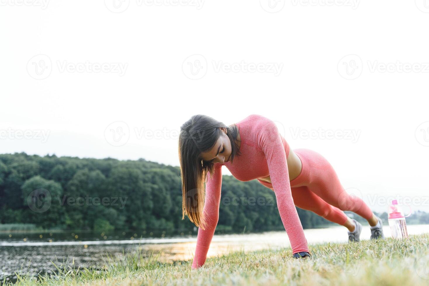 empujar UPS o prensa UPS ejercicio por joven mujer. niña trabajando fuera en césped crossfit fuerza formación en el resplandor de el Mañana Dom en contra un blanco cielo con espacio de copia. mezclado carrera asiático caucásico modelo. foto