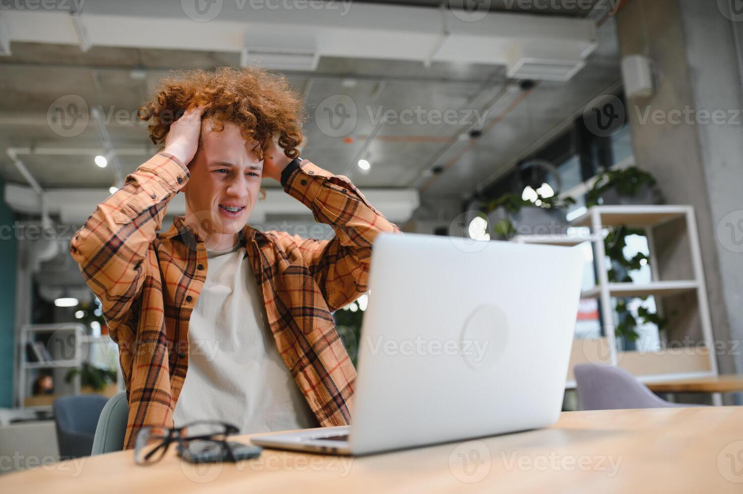 Young happy male freelancer in casual clothes sitting in cafe with laptop and using mobile phone. photo