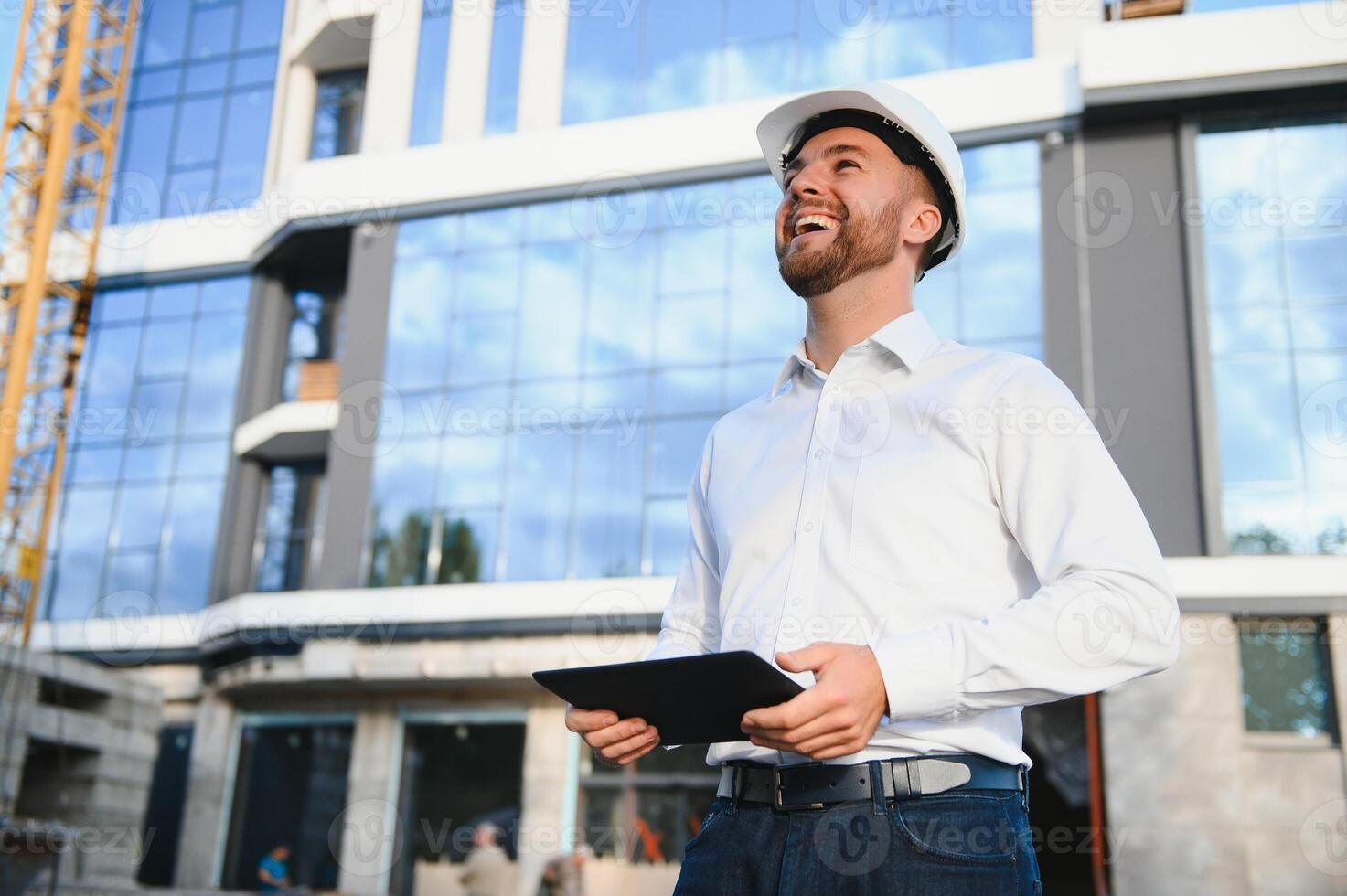 Engineer next to building cranes. Concept - large construction project. Architect directs the construction process. Drawings and tablet in the hands. photo