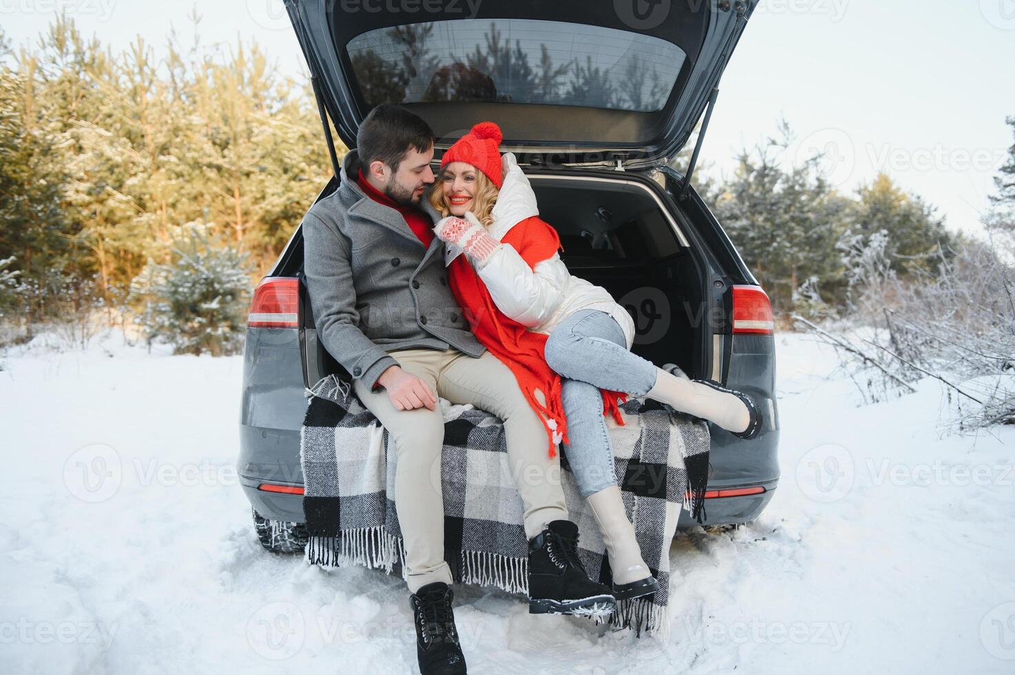 Happy couple sitting in open car back, having stop off. Romantic traveling concept. Winter forest. photo