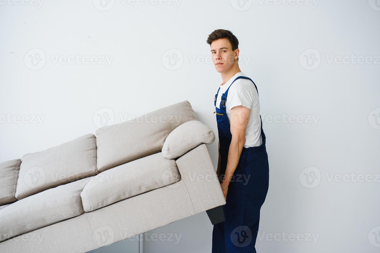 Loader moves sofa, couch. worker in overalls lifts up sofa, white background. Delivery service concept. Courier delivers furniture in case of move out, relocation. photo