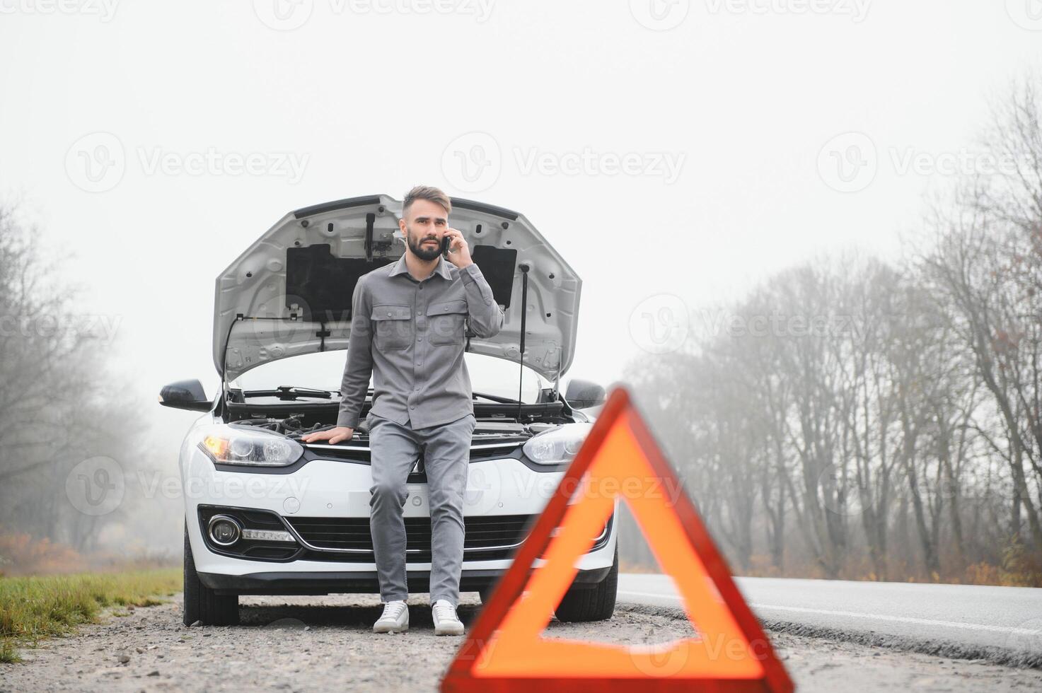 Sad driver calling car service, opening hood, having engine problem standing near broken car on the road. Car breakdown concept photo