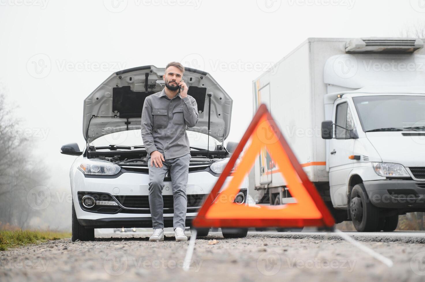 Sad driver calling car service, opening hood, having engine problem standing near broken car on the road. Car breakdown concept photo