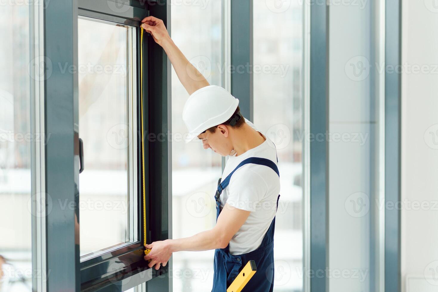 Workman in overalls installing or adjusting plastic windows in the living room at home photo