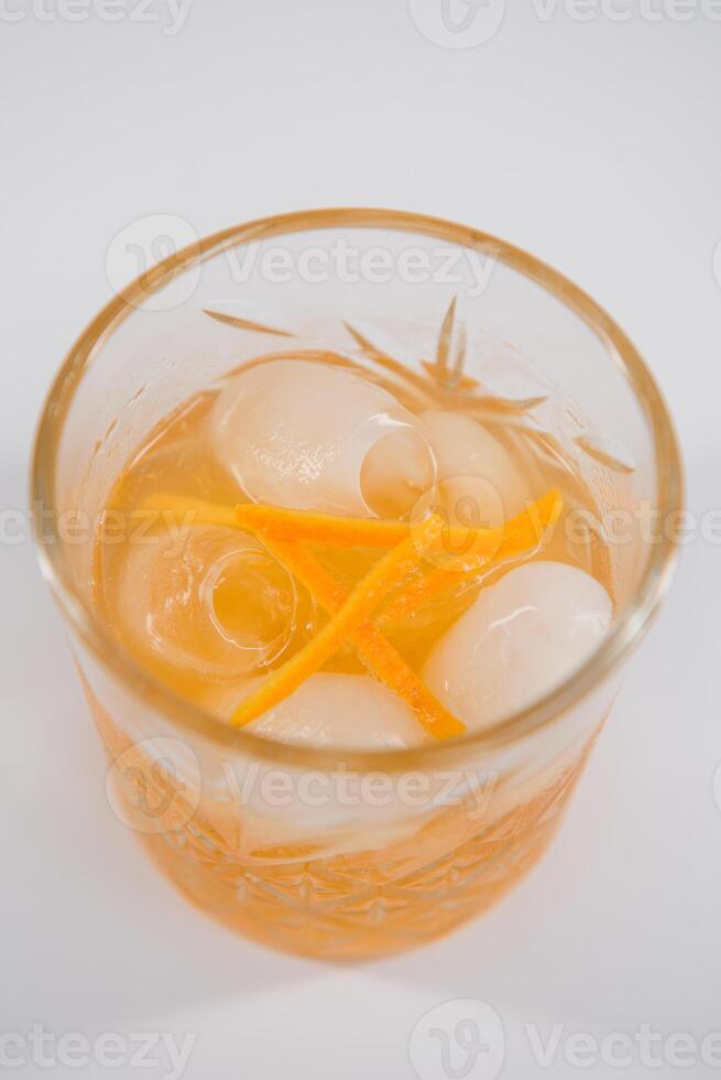 Glass of Boulevardier cocktail with big ice cube and orange zest, classic cocktail Boozy Boulevardier with Orange and Vermouth isolated on white background photo