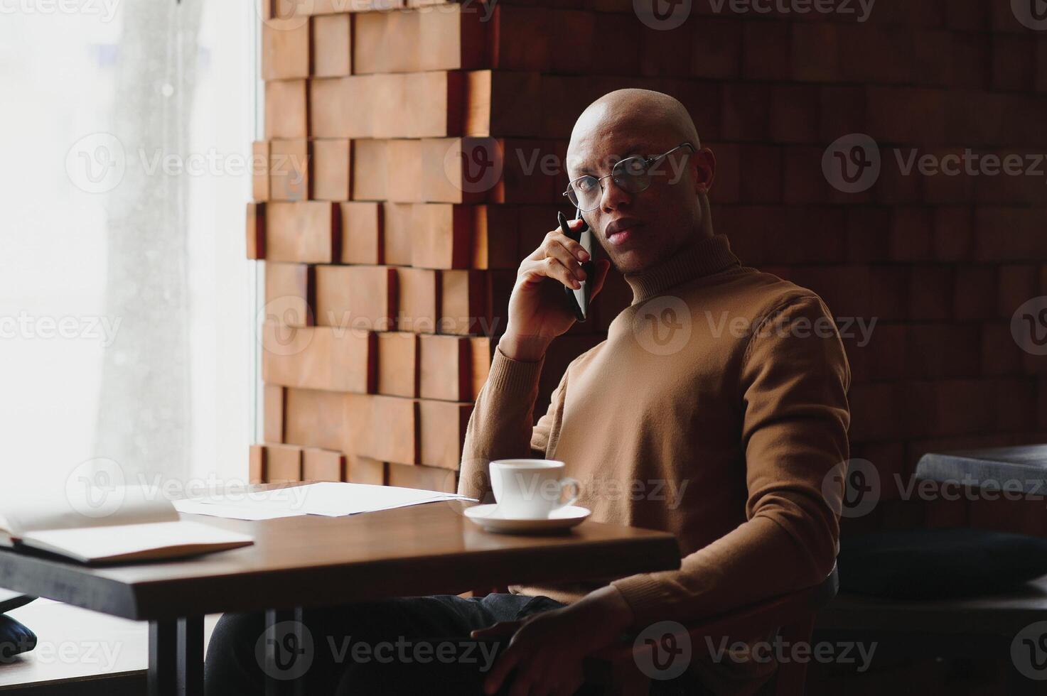 African-Ameican entrepreneur wearing shirt with rolled up sleeves looking through window with thoughtful and serious face expression, feeling nervous before meeting with business partners at cafe. photo