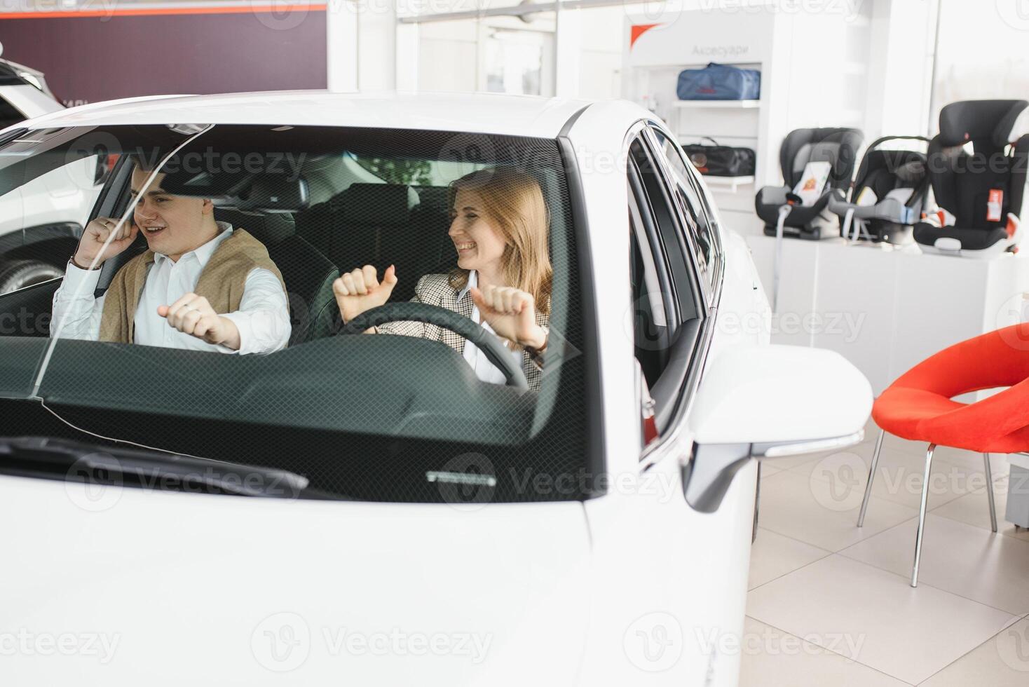 visitando coche concesión. hermosa Pareja es mirando a cámara y sonriente mientras sentado en su nuevo coche. foto