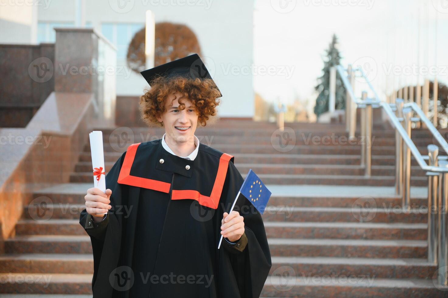 excited graduate student in gown with risen hands holding diploma. photo