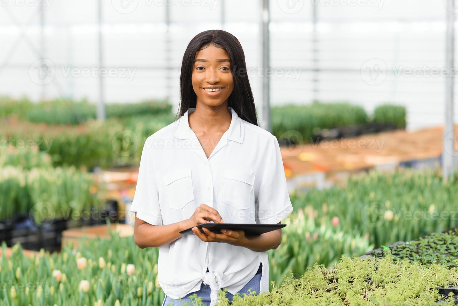 Beautiful young smiling african american girl, worker with flowers in greenhouse. Concept work in the greenhouse, flowers. photo