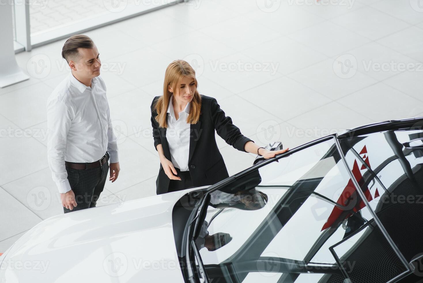 Visiting car dealership. Beautiful couple is holding a key of their new car and smiling, girl is kissing her husband in cheek. photo