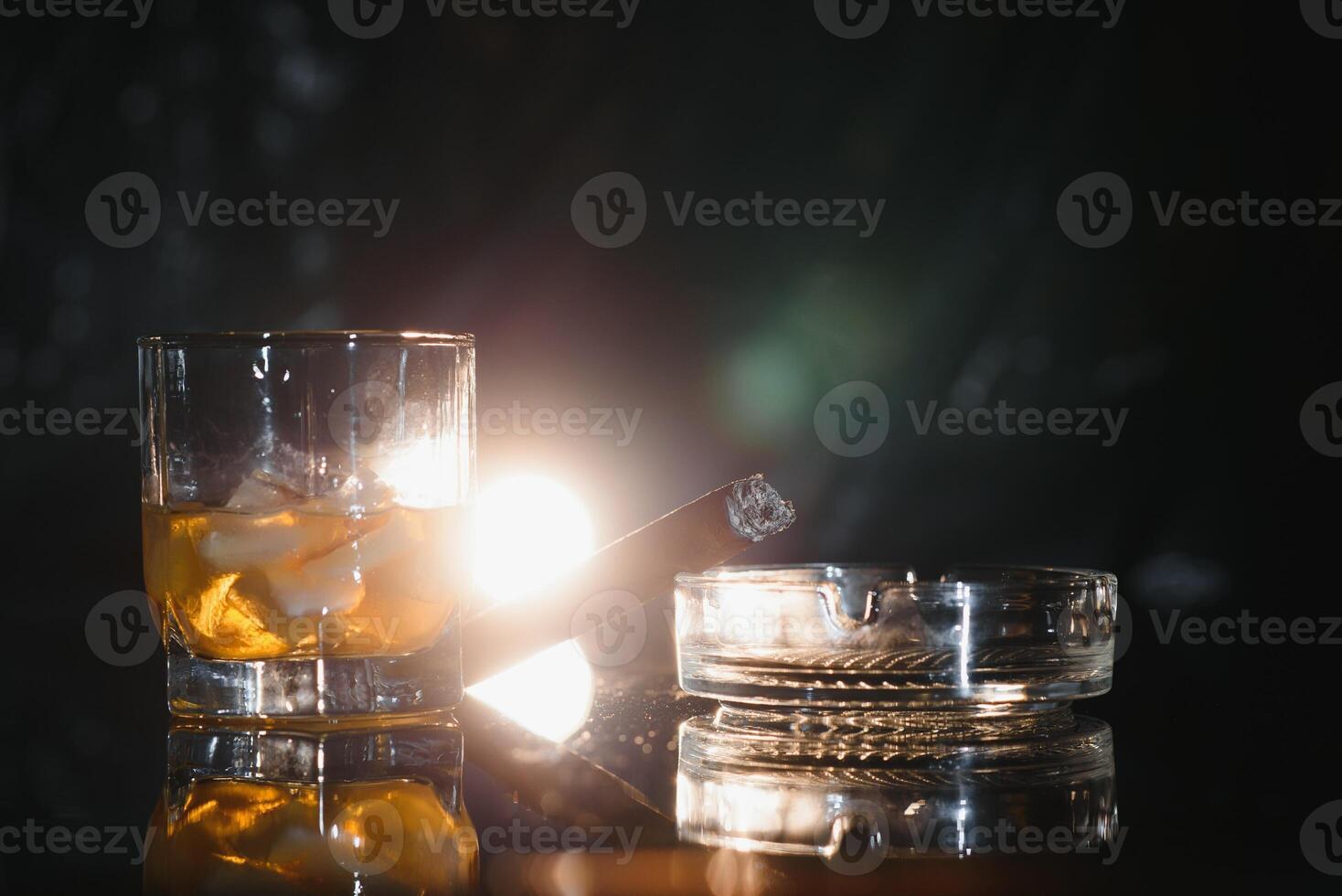 A glass of whiskey or Bourbon with ice cubes and a cigar on a black slate with smoke photo