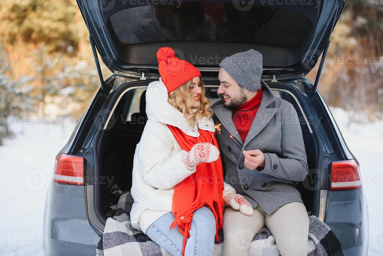 Smiling together. Nice couple have weekend at countryside at winter time. Sitting on the rear part of modern car. photo