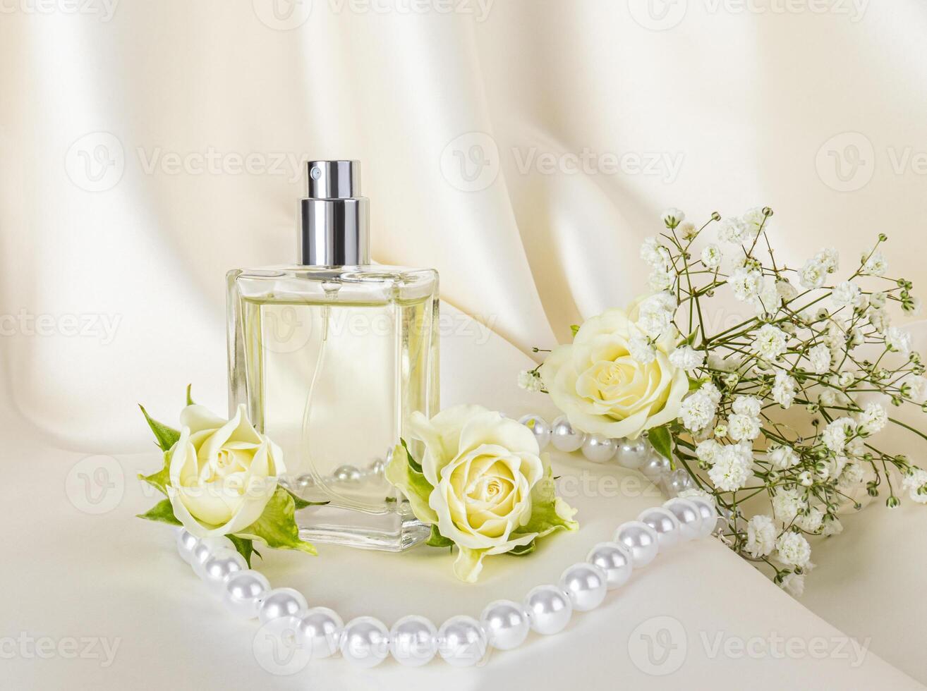 Elegant bottle of cosmetic spray, perfume on beige satin fabric with delicate roses and white pearls. Product presentation. Blank lay. photo