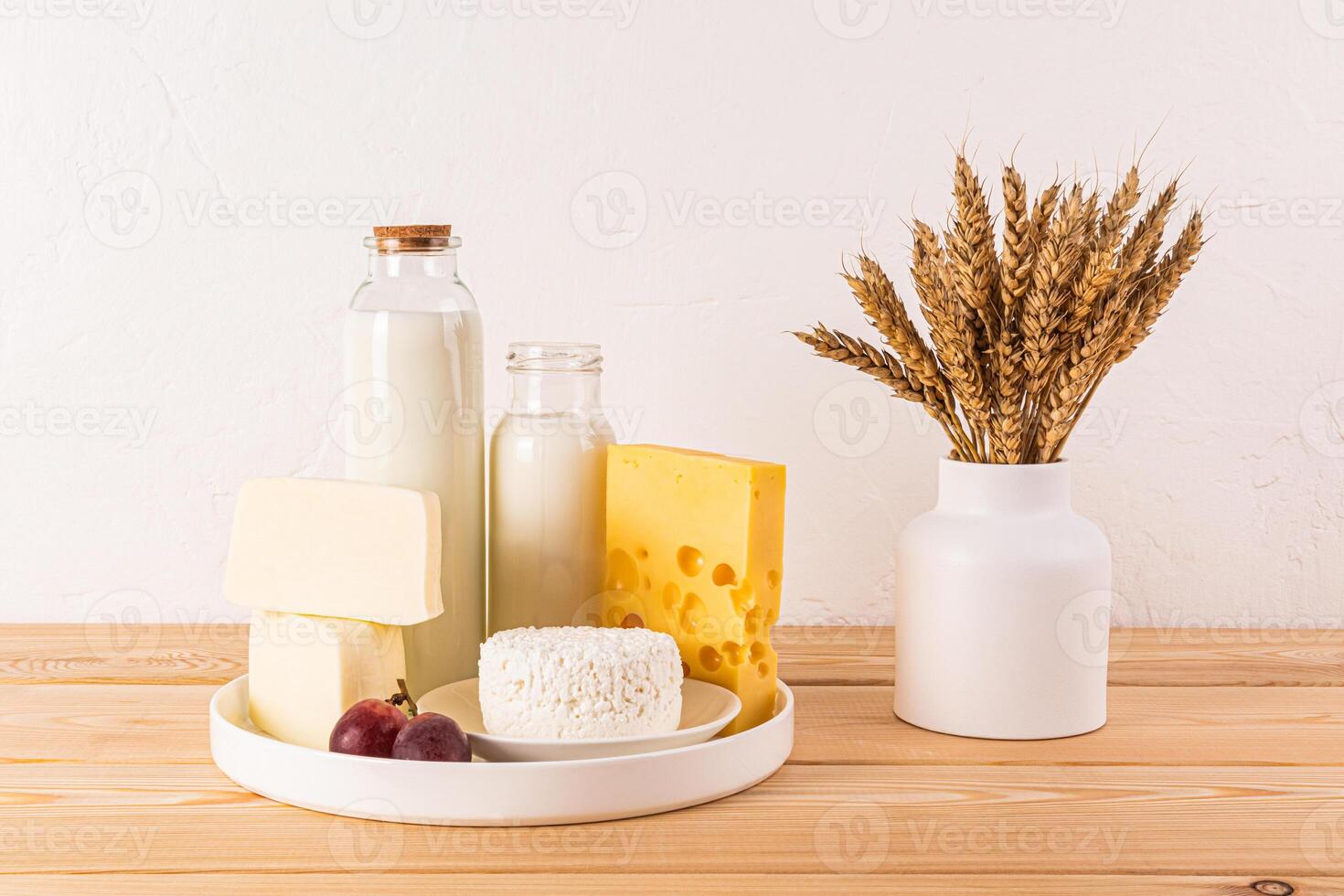 Fresh dairy products, cheese, bottle milk on a white dish and a wooden table with a vase with ears of corn. Concept of the Jewish holiday of Shavuot. photo
