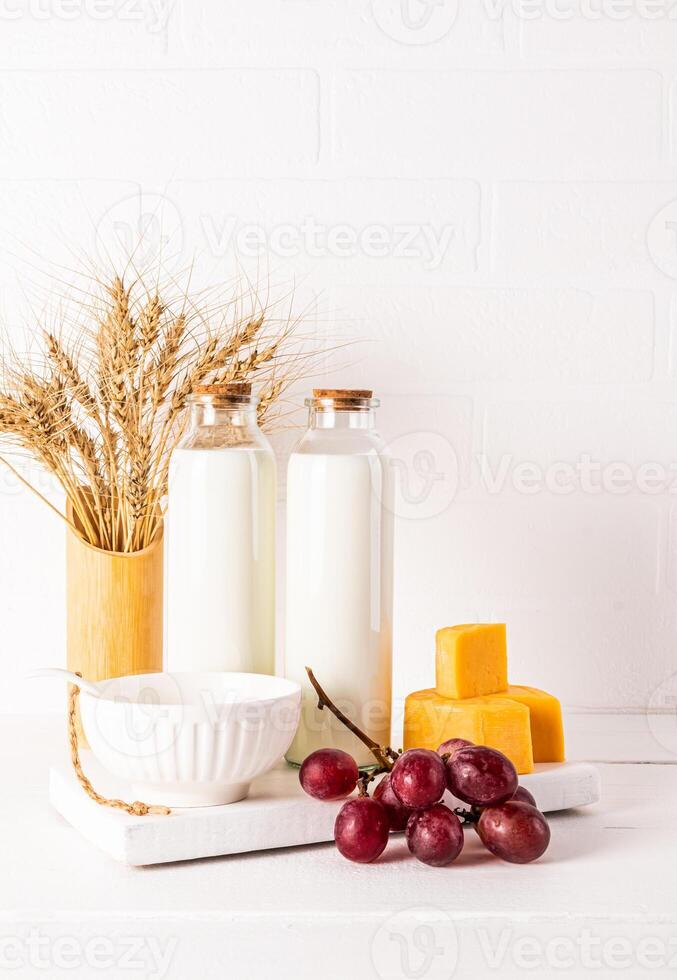 A beautiful still life for the holiday of Jewish Shavuot. Fresh dairy products, bunch of grapes and ears of bread on white vertical background. photo