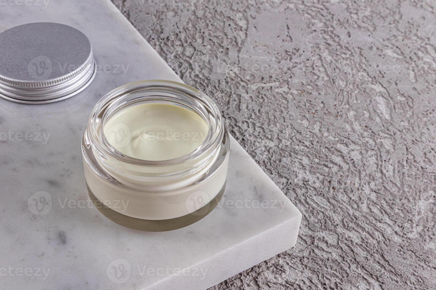 Delicate texture of nourishing olive or aloe vera in a glass cosmetic jar on a white marble podium and a grey cement. A copy space. layout. packaging. photo