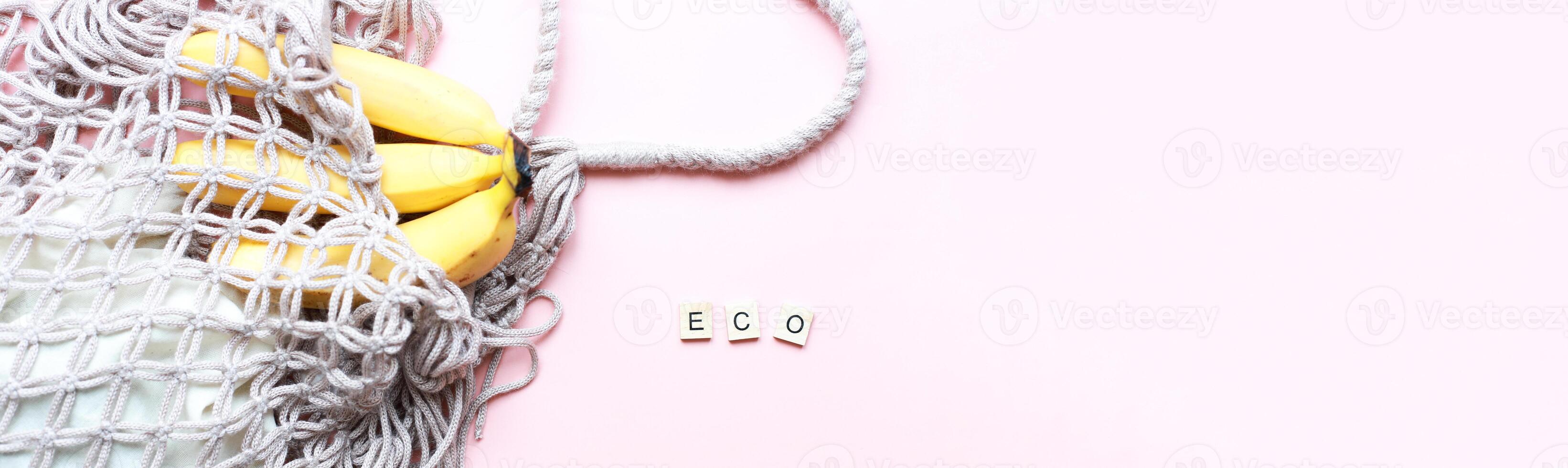 Banner Flat lay bananas in a mesh bag. The word eco from wooden letters on a pink background. Zero waste photo