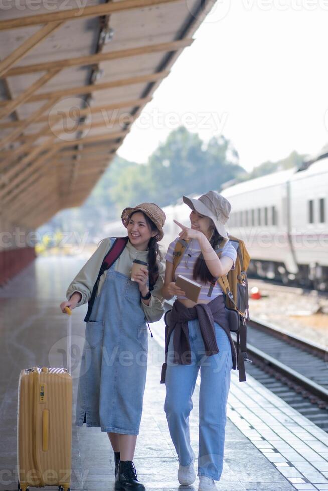 two young asian friends girls with backpacks at railway station waiting for train, Two beautiful women walking along platform at train station photo