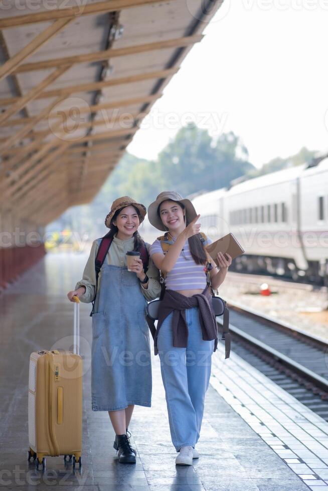 two young asian friends girls with backpacks at railway station waiting for train, Two beautiful women walking along platform at train station photo