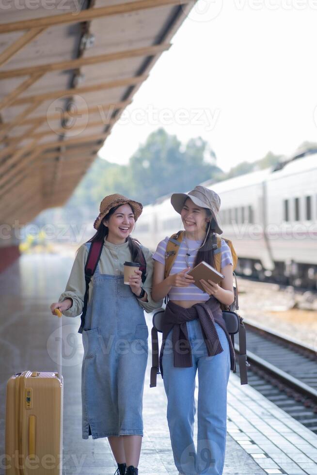 two young asian friends girls with backpacks at railway station waiting for train, Two beautiful women walking along platform at train station photo