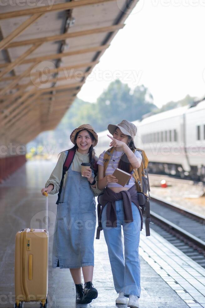 two young asian friends girls with backpacks at railway station waiting for train, Two beautiful women walking along platform at train station photo