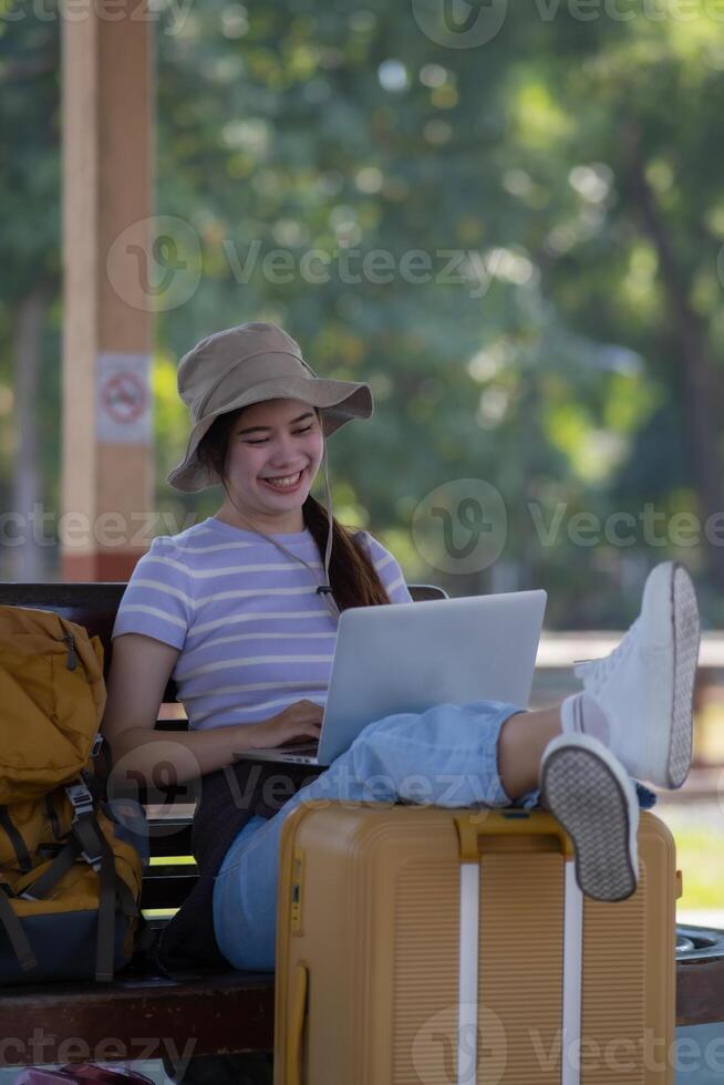 Girl using a laptop while waiting in a train station, Girl on train station with luggage working on laptop computer, laptop in use, sits with a suitcase photo