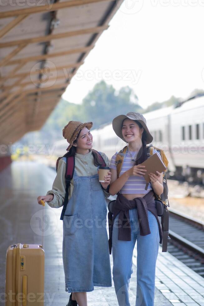 two young asian friends girls with backpacks at railway station waiting for train, Two beautiful women walking along platform at train station photo