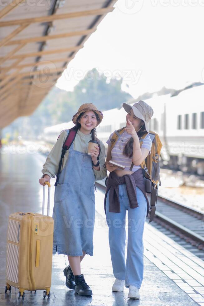 two young asian friends girls with backpacks at railway station waiting for train, Two beautiful women walking along platform at train station photo
