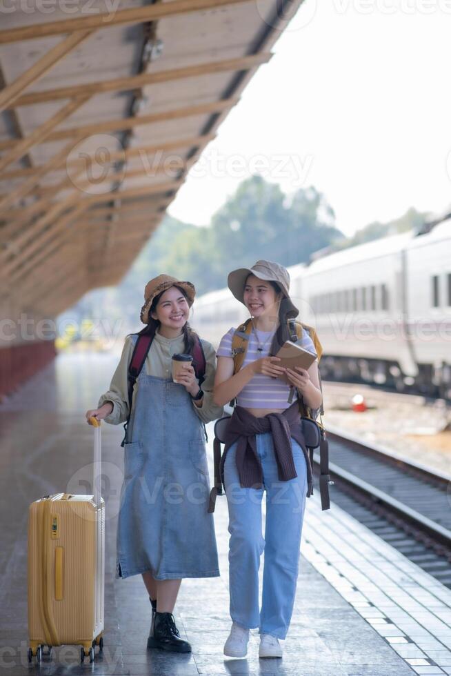 two young asian friends girls with backpacks at railway station waiting for train, Two beautiful women walking along platform at train station photo