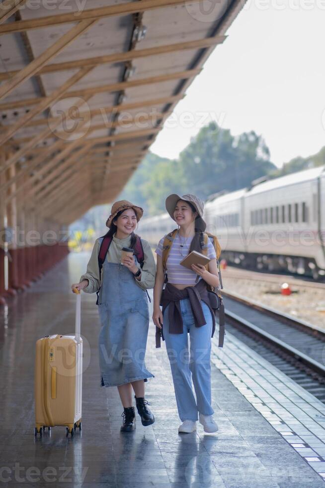 two young asian friends girls with backpacks at railway station waiting for train, Two beautiful women walking along platform at train station photo