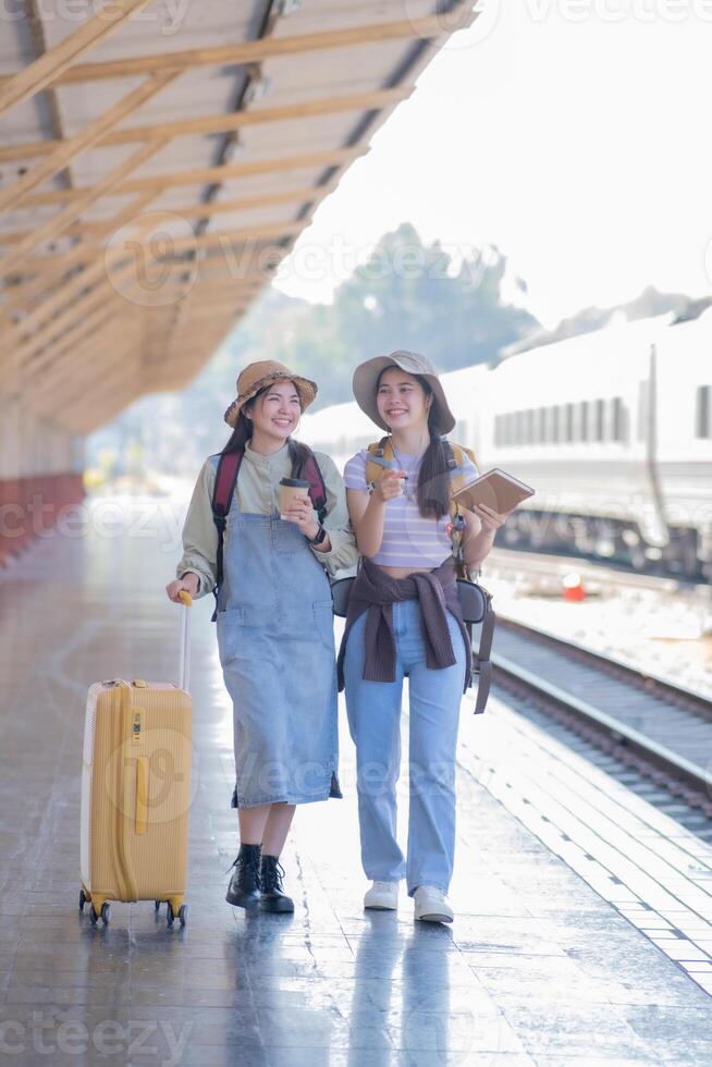 two young asian friends girls with backpacks at railway station waiting for train, Two beautiful women walking along platform at train station photo