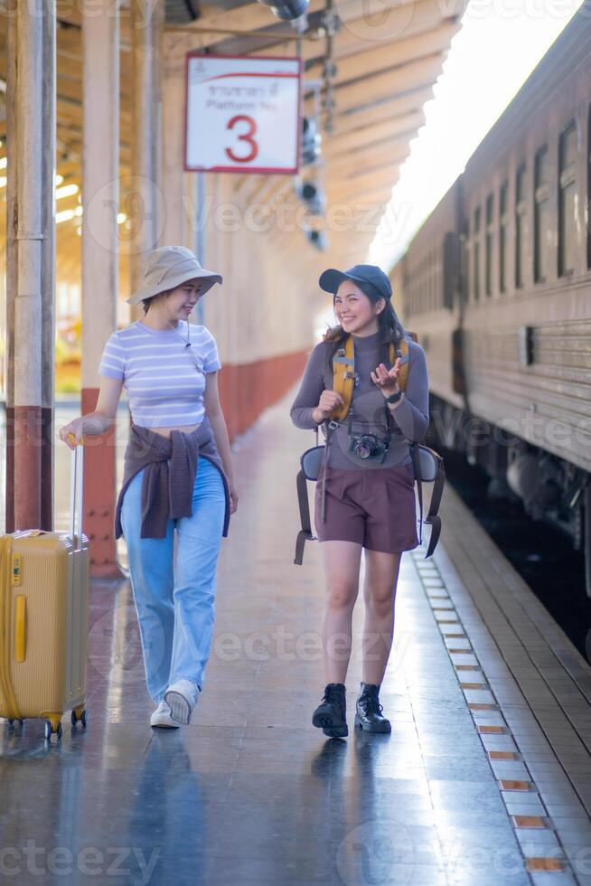 two young asian friends girls with backpacks at railway station waiting for train, Two beautiful women walking along platform at train station photo