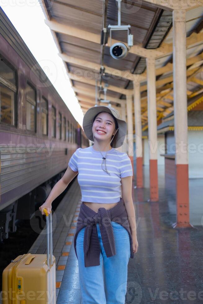 joven mujer con maleta murga a el metro estación mientras el tren llega, turismo y viaje en el verano. vacaciones para el alumno. trabajo y viaje foto