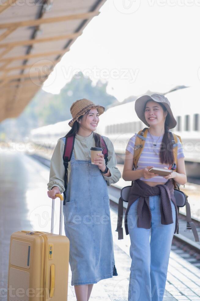 two young asian friends girls with backpacks at railway station waiting for train, Two beautiful women walking along platform at train station photo