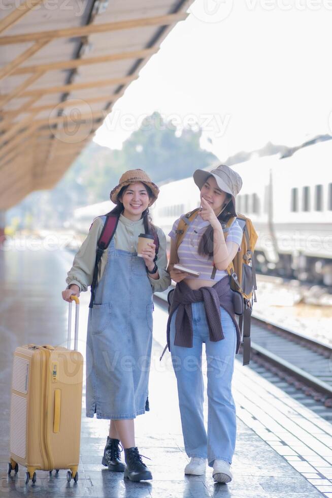 two young asian friends girls with backpacks at railway station waiting for train, Two beautiful women walking along platform at train station photo