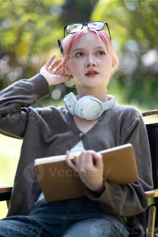 Young Happy Asian artist woman drawing book and wearing headphone, the artist paints in the garden photo