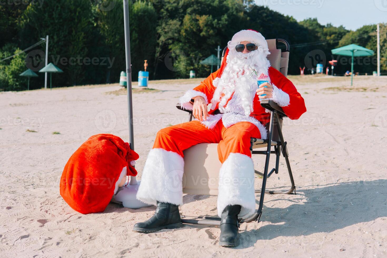 Santa Claus in sunglasses drinks a cocktail while lying on a sun lounger on the lake beach. Santa in the tropics photo