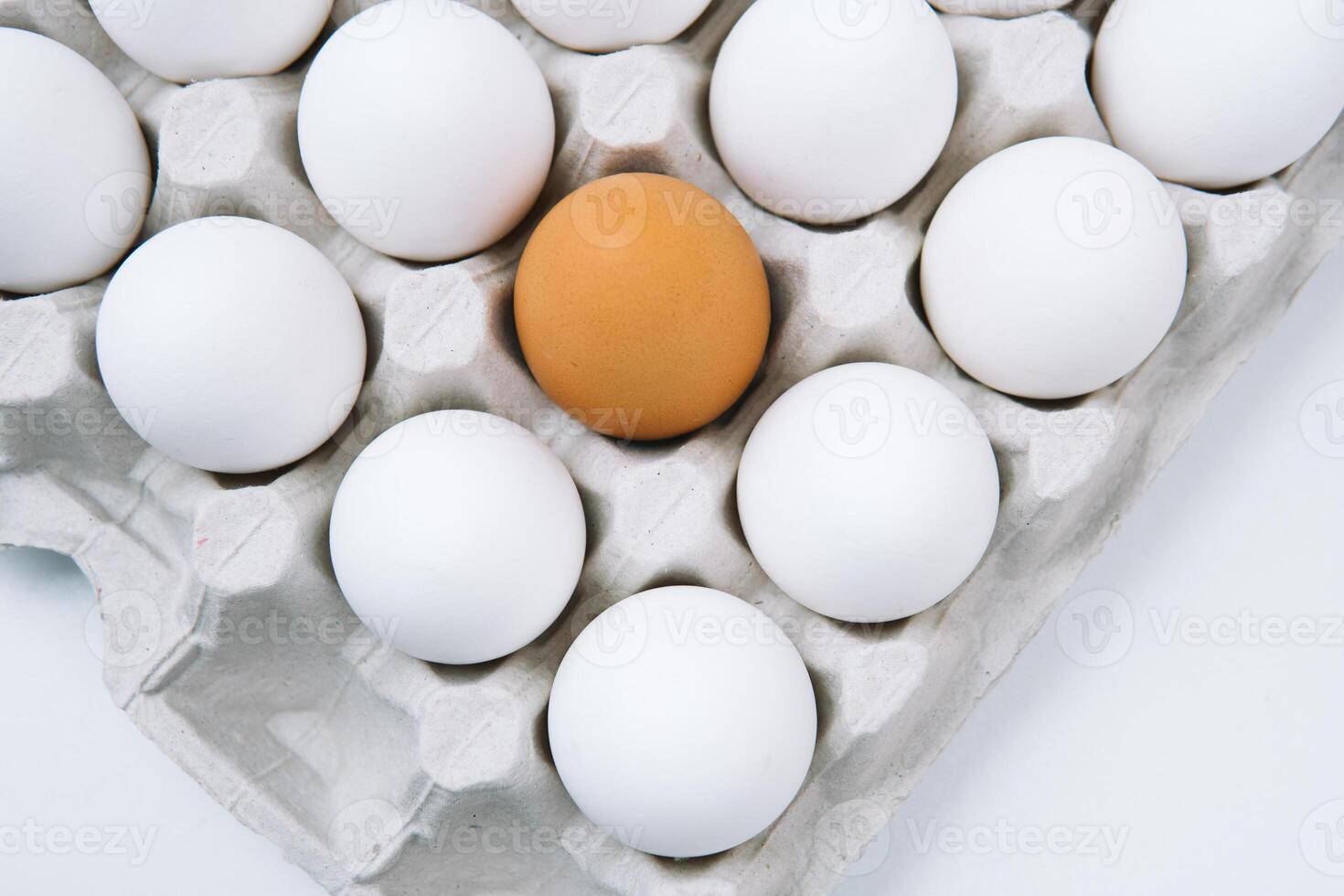 White raw chicken eggs and alone brown egg in a tray top view photo