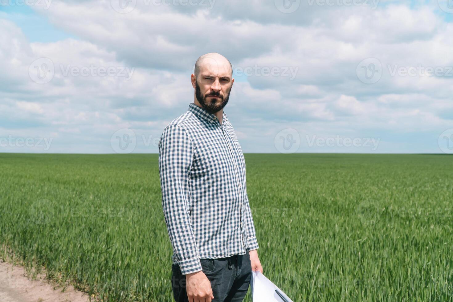 Portrait of farmer man with beard looking to camera in wheat field. Farmer examines the field of cereals photo