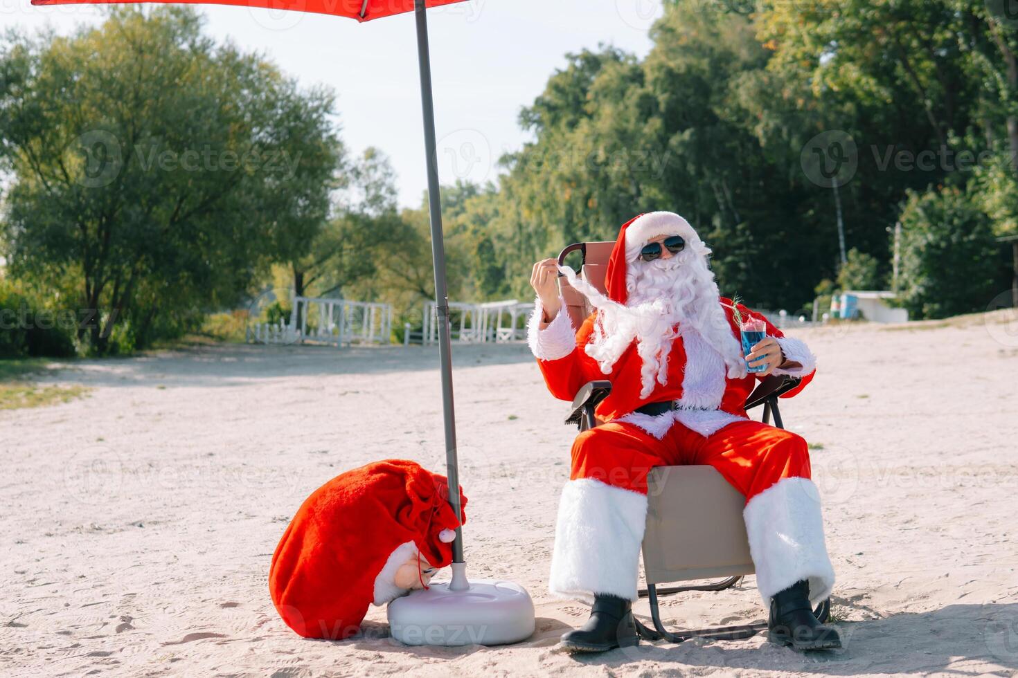 Santa Claus in sunglasses drinks a cocktail while lying on a sun lounger on the lake beach. Santa in the tropics photo