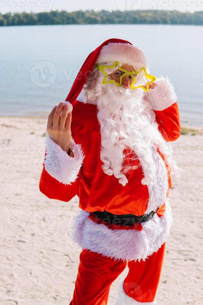 Santa Claus in funny glasses on the lake beach. Travel and vacation concept photo